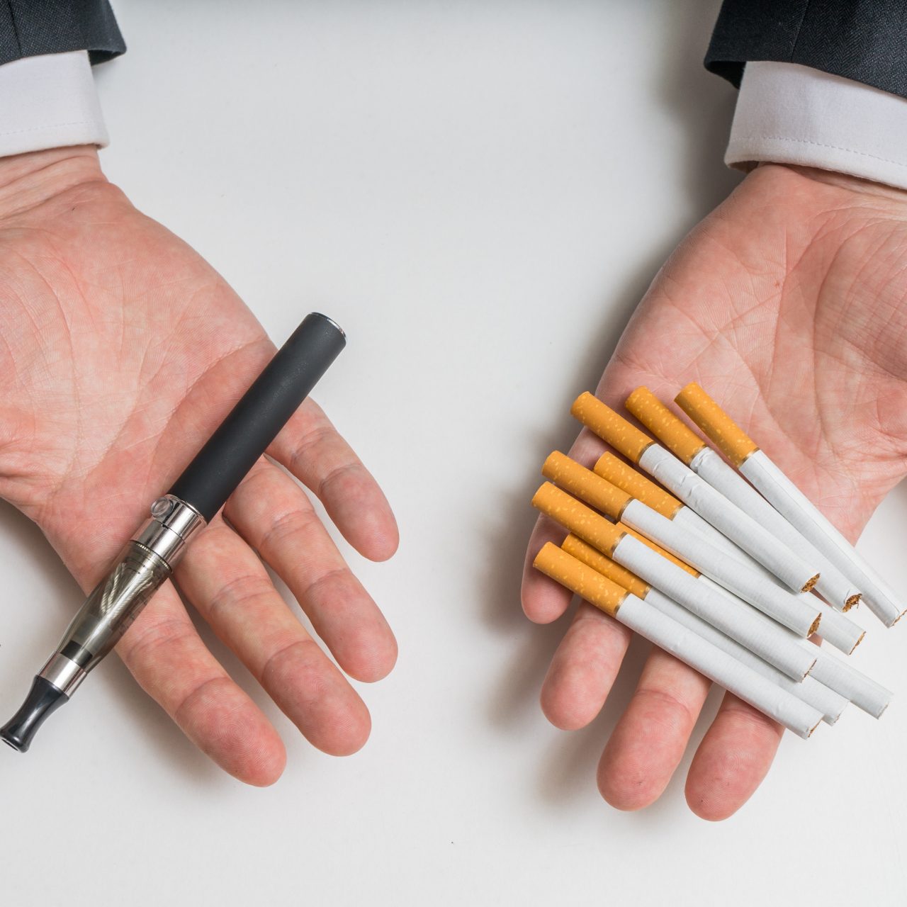 Hands are holding electronic vaporizer and conventional tobacco cigarettes and comparing them.
